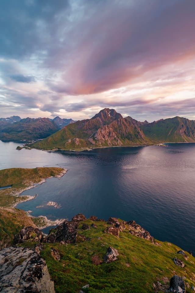 A scenic landscape featuring a rugged coastline with mountains, surrounded by calm water under a dramatic, colorful sky