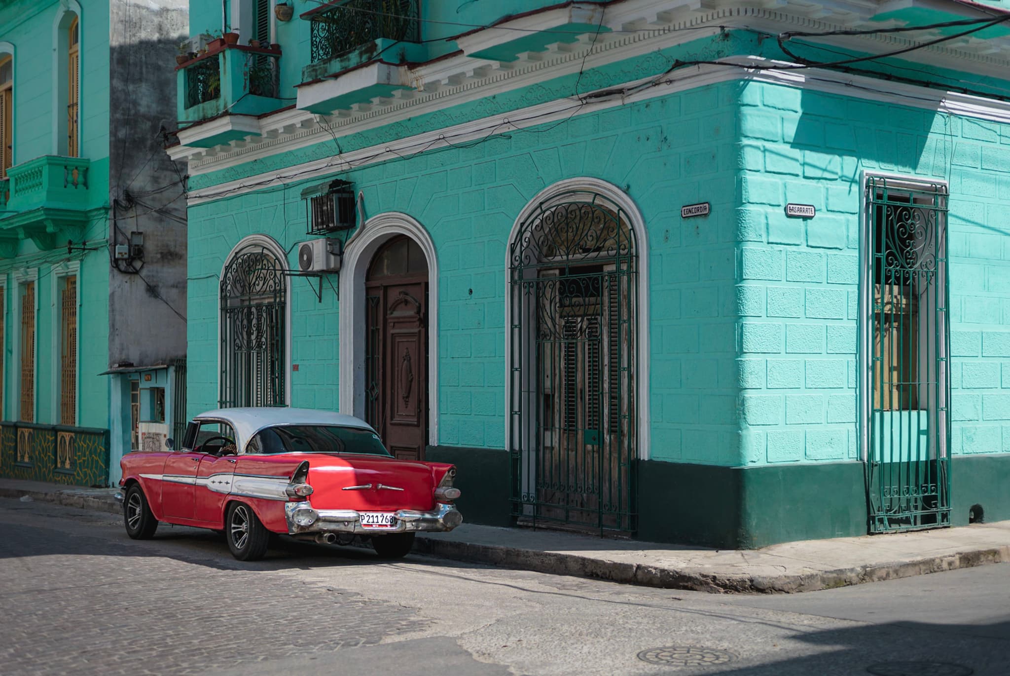 Red and white vintage car parked beside a turquoise corner building on a quiet cobblestone street