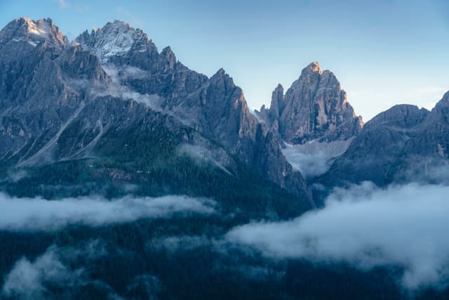 A mountain range with jagged peaks, partially covered by clouds, under a clear blue sky