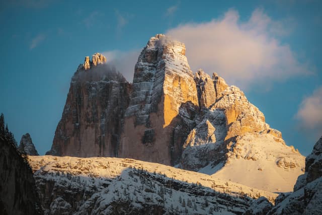 Snow-dusted rocky mountain peaks glowing in warm sunset light beneath a partly cloudy sky