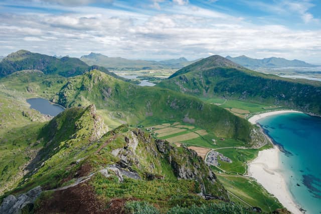 A scenic landscape featuring lush green mountains, a sandy beach, and a clear blue sea under a partly cloudy sky