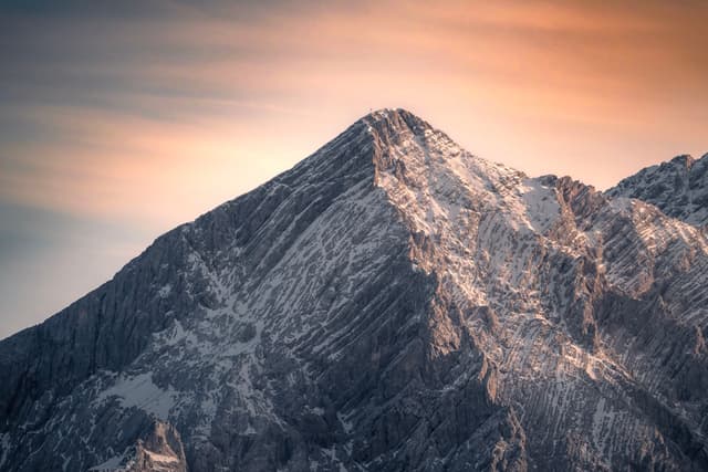 Snow-dusted mountain peak under a warm, glowing sunset sky
