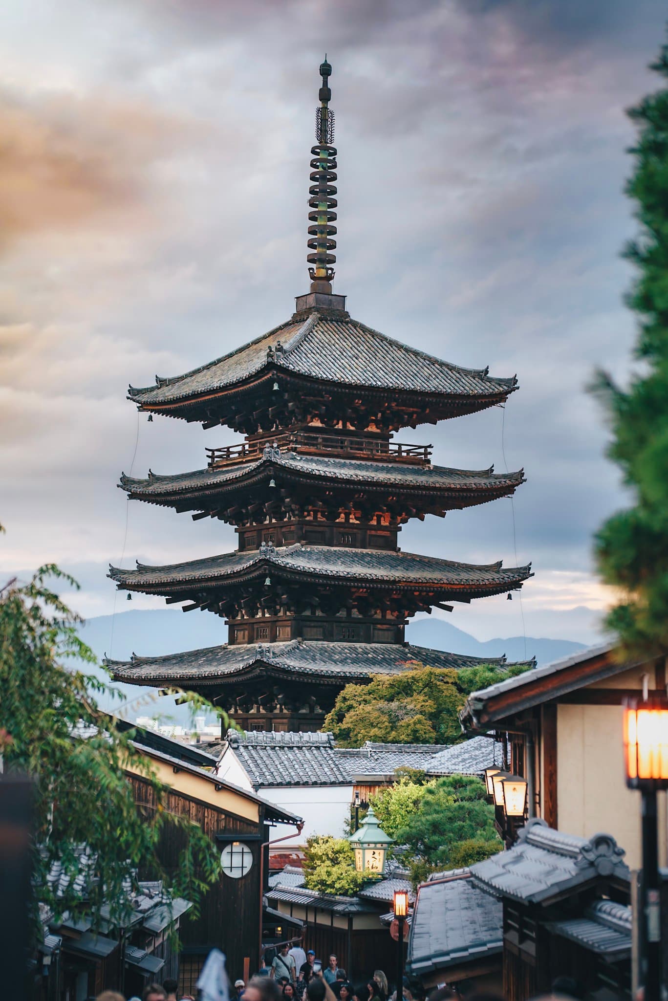 traditional pagoda rising above narrow street and rooftops at dusk with people walking below