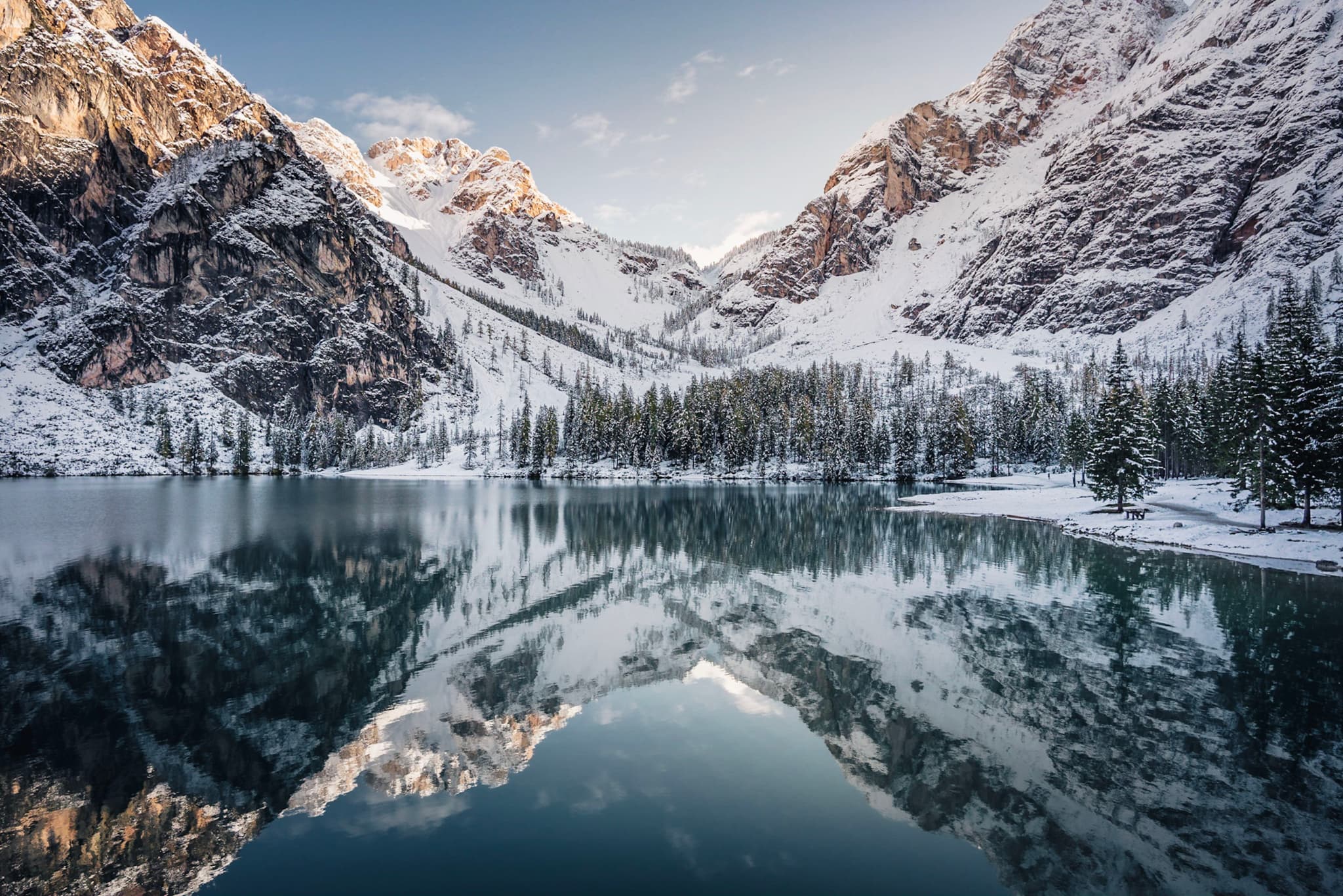 Snow-covered mountains and pine forest reflected perfectly in a calm alpine lake at sunrise