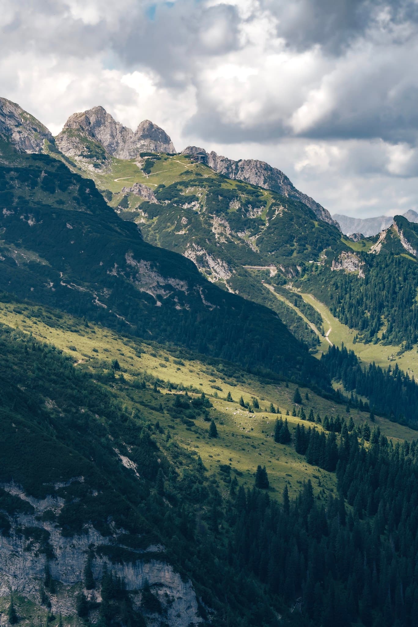 Layered green mountain slopes with a sunlit valley and scattered clouds overhead