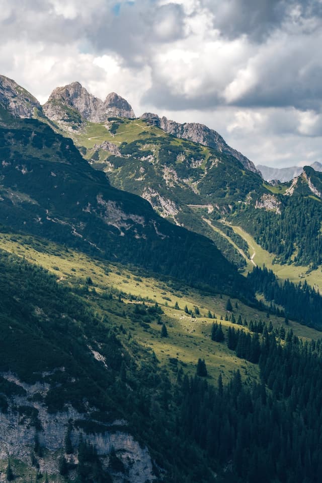 Layered green mountain slopes with a sunlit valley and scattered clouds overhead