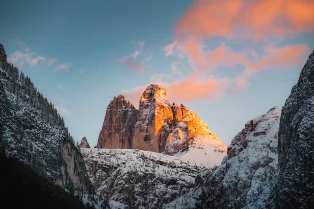 Snow-covered mountain peak glowing with warm alpenglow under soft pink clouds at sunset