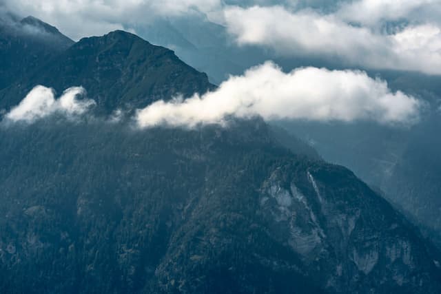 A mountain range partially covered by clouds, with a misty atmosphere and rugged terrain