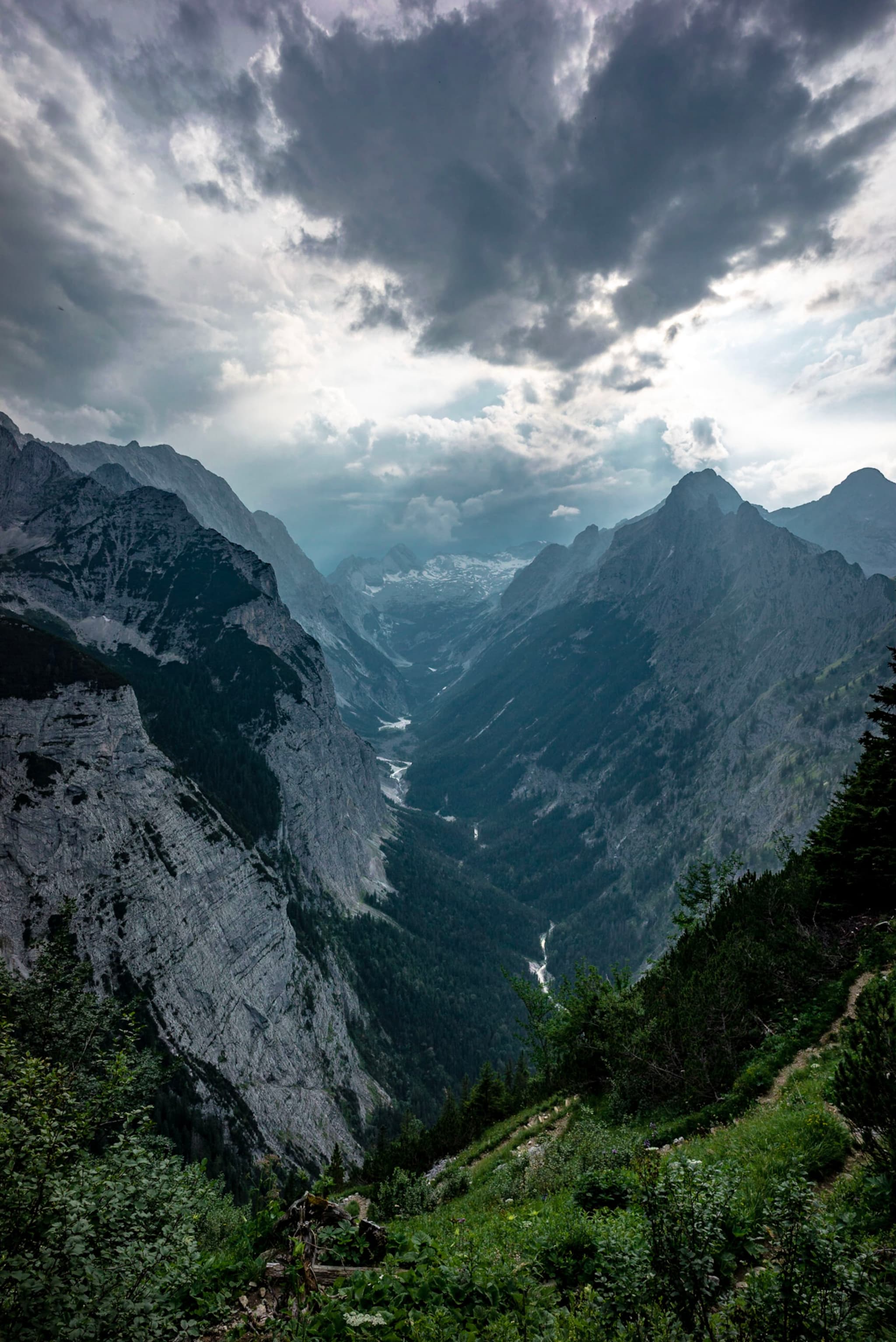 A dramatic mountain landscape with steep cliffs and a narrow valley, under a cloudy sky