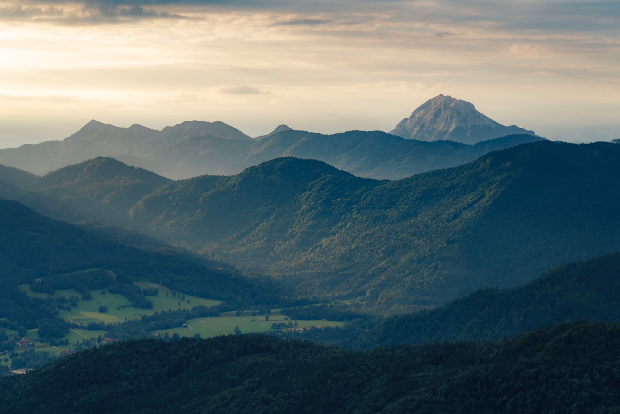 Sunlit valley and layered mountain ridges with a distant snowcapped peak under a hazy sky