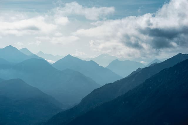 Multiple blue-toned mountain ridges receding into the mist beneath a cloudy sky