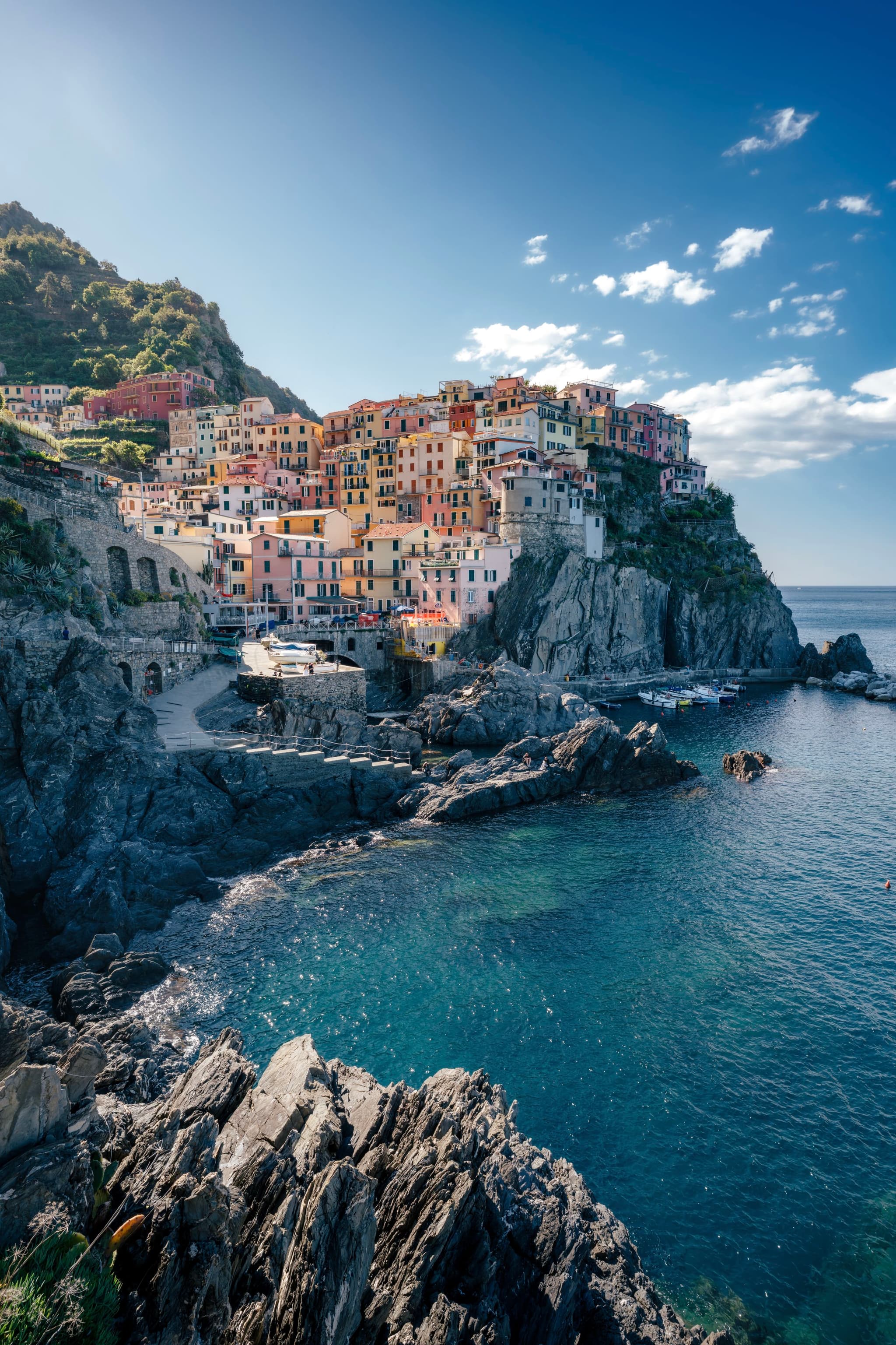 A coastal village with colorful buildings perched on a rocky cliff overlooking a clear blue sea under a partly cloudy sky