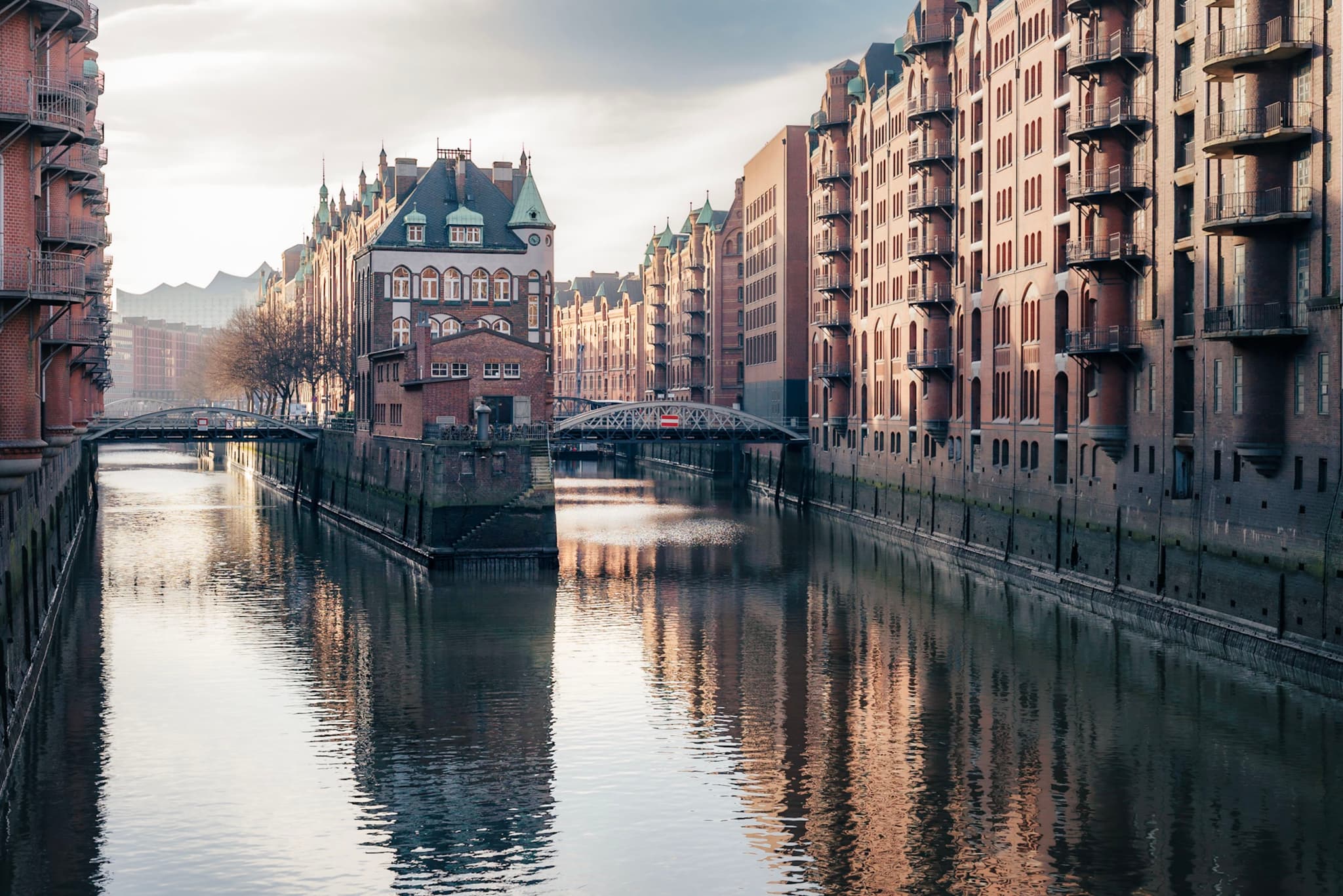 Historic brick warehouses lining a calm canal with a central gabled building reflected in the water at dawn