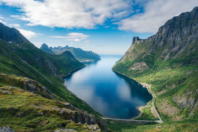 Narrow blue fjord stretching between steep green mountains under a partly cloudy sky
