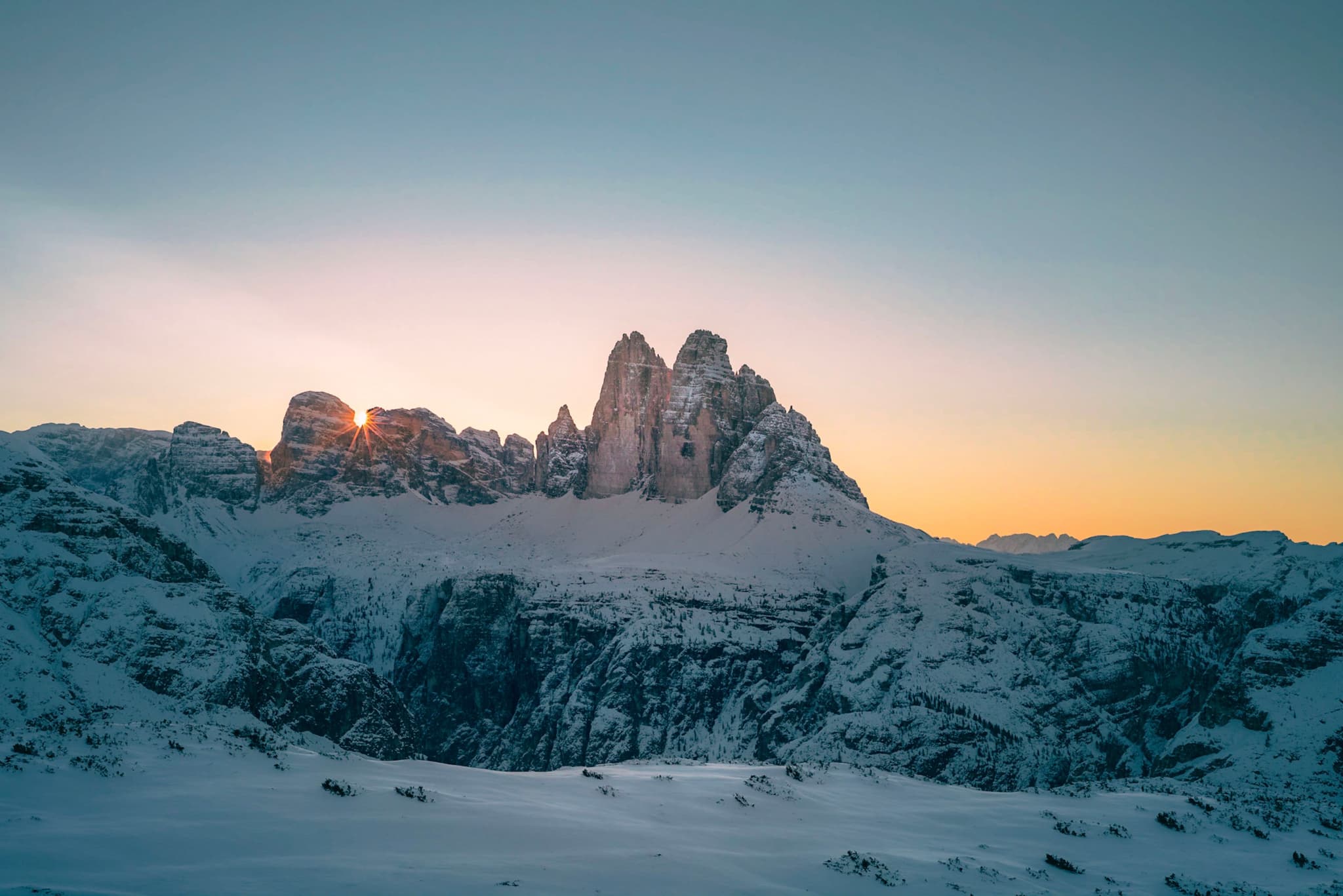 Snow-covered mountain peaks glowing in the soft light of sunrise against a clear sky