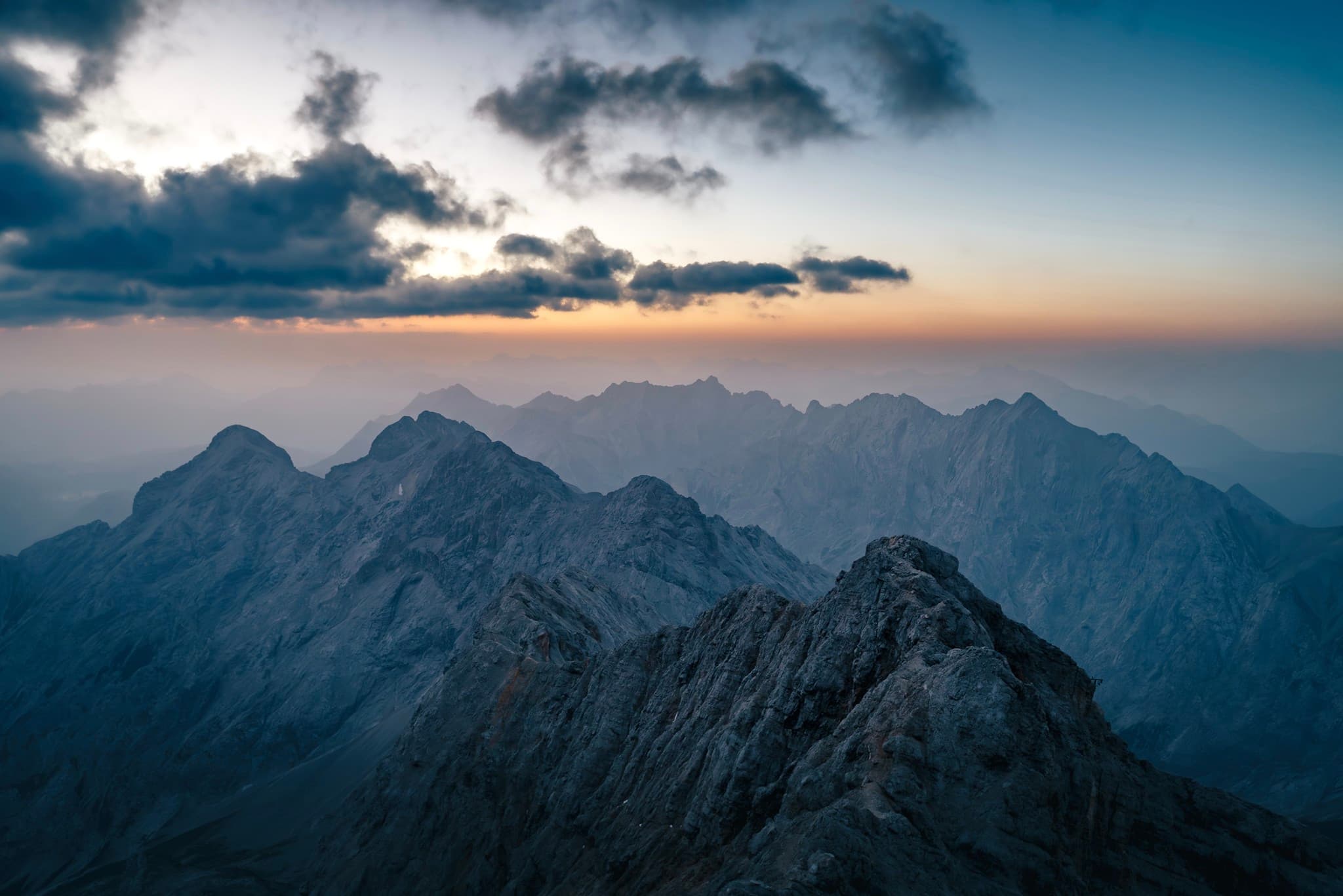 Jagged mountain ridges fading into distant haze under a colorful dusk sky with scattered clouds