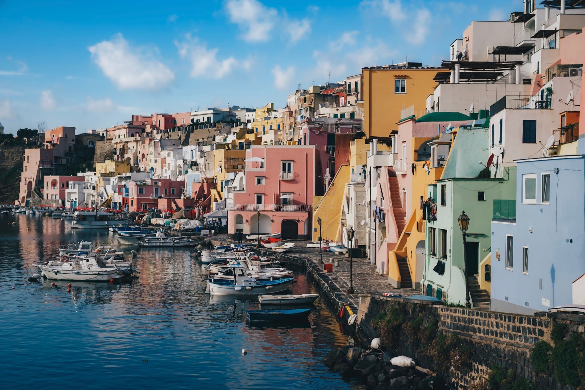 colorful stacked waterfront houses lining a calm harbor filled with small boats under a bright blue sky