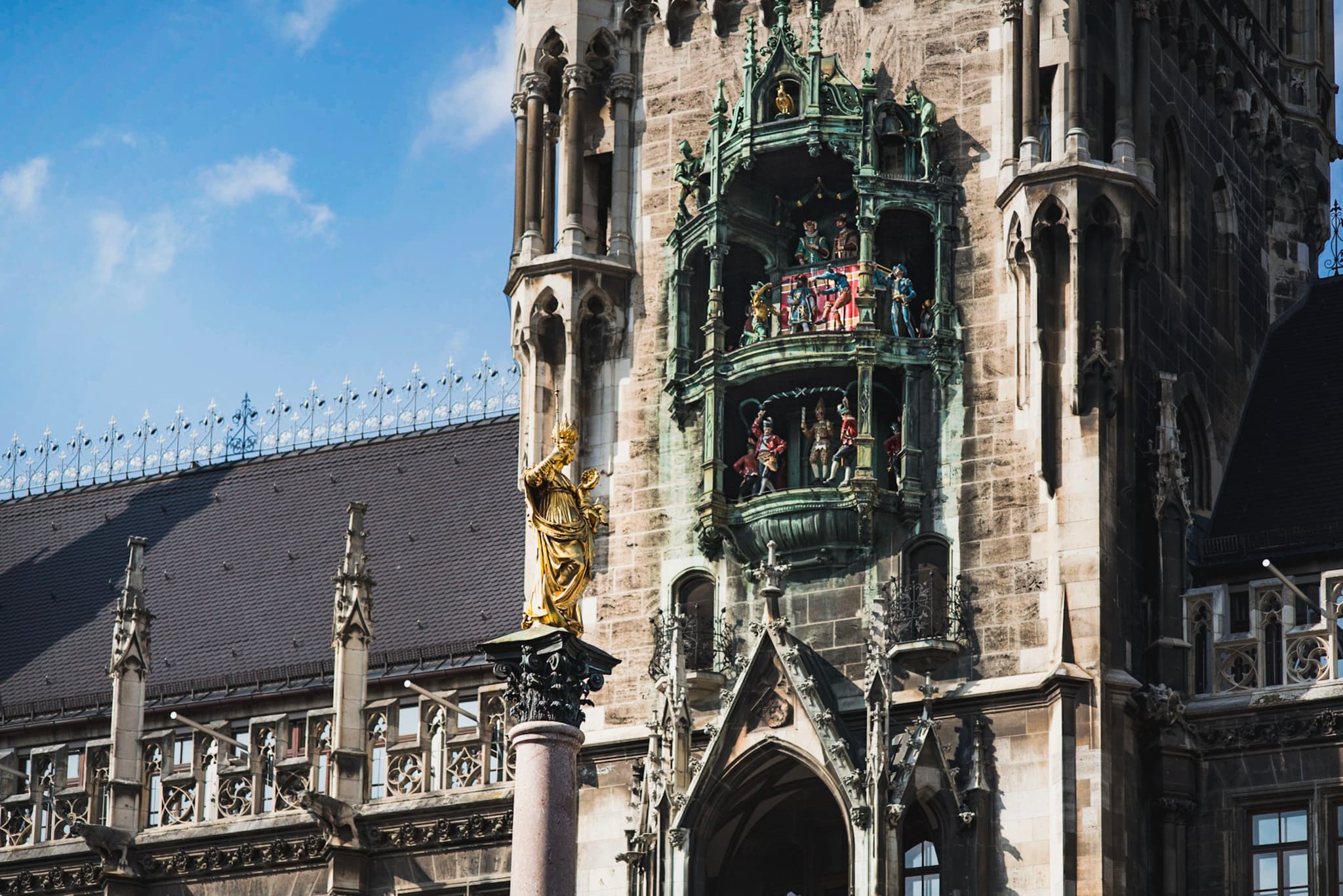 Ornate Gothic-style clock tower with detailed statues and figurines set into an elaborate façade under a blue sky