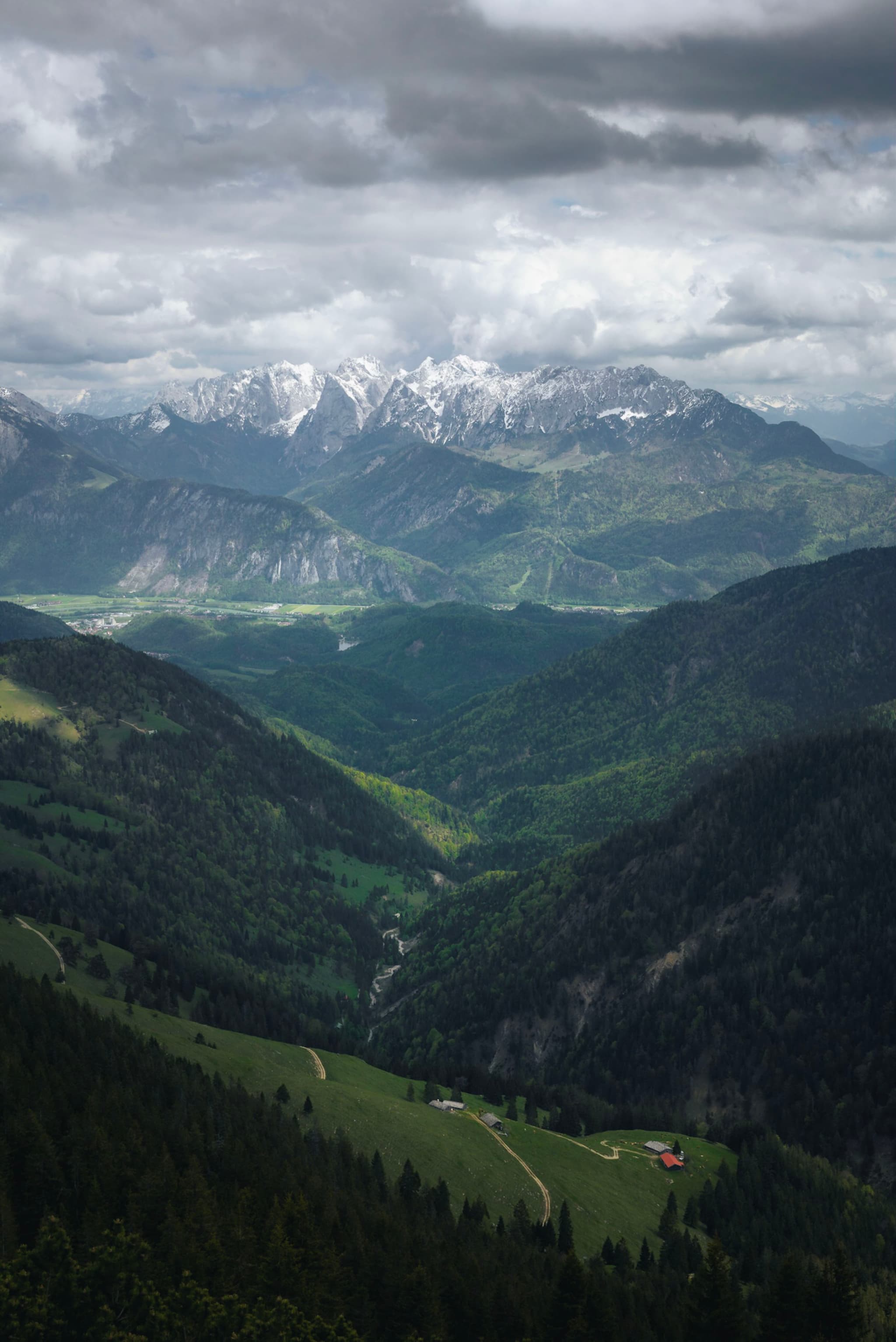 Layered green valleys leading toward distant snowcapped mountains under a dramatic, overcast sky
