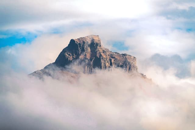Jagged mountain peak emerging through a thick layer of clouds under a bright sky