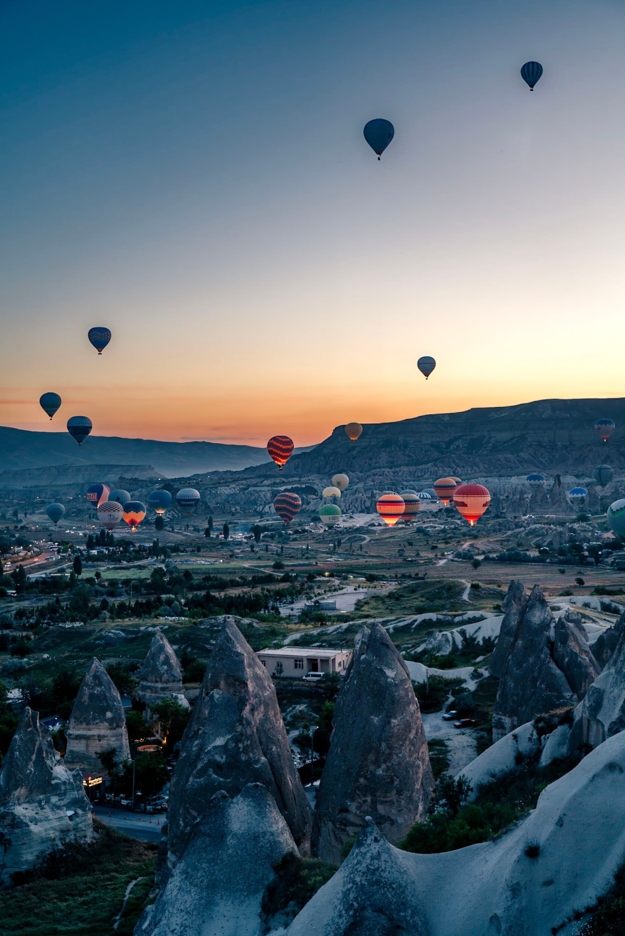 Hot air balloons floating over a rocky landscape at sunrise, with a clear sky and distant mountains