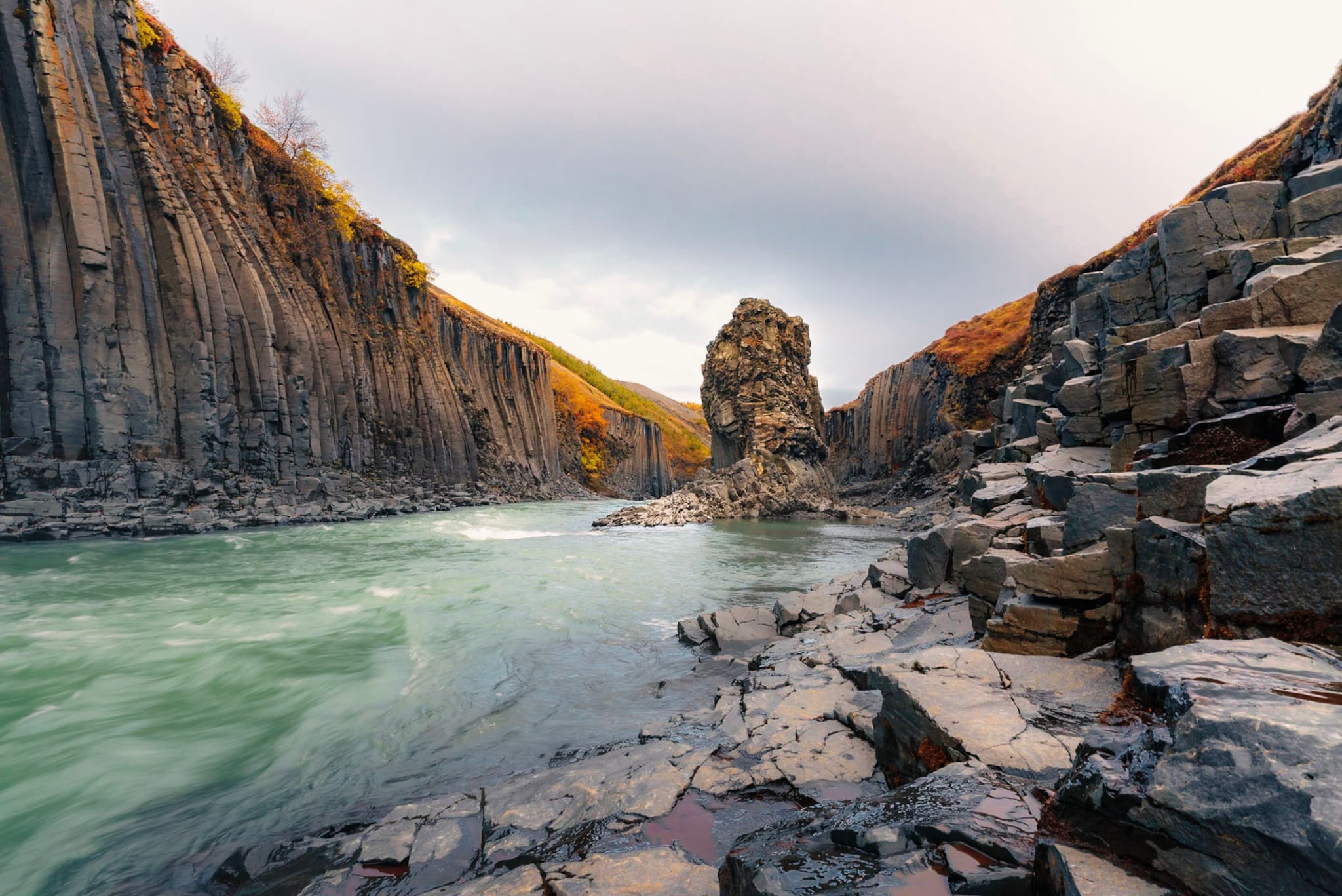 turquoise river winding between steep basalt canyon walls with scattered rocks under a soft overcast sky