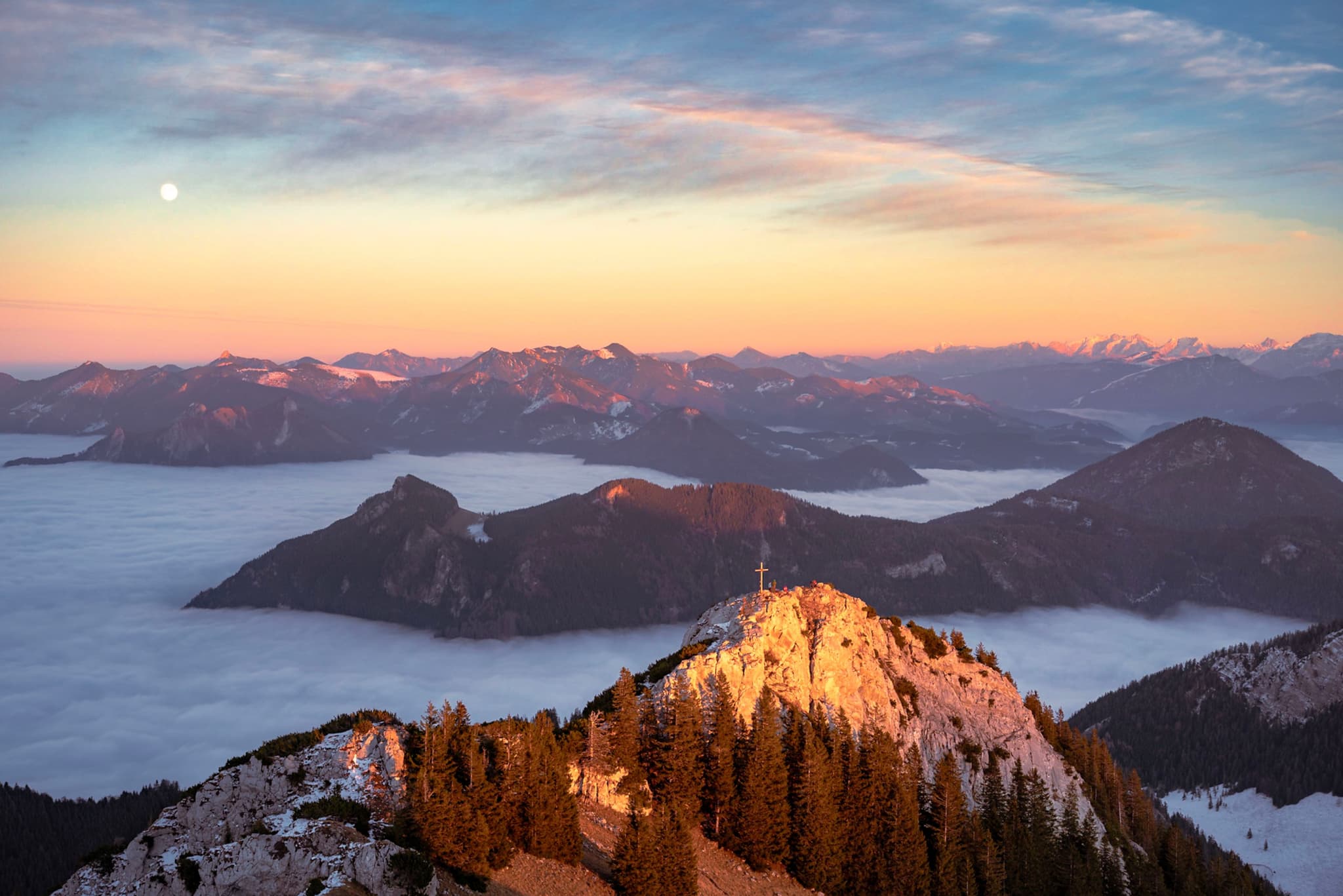 snow-dusted mountain ridge glowing in sunrise light above a sea of clouds and distant ranges