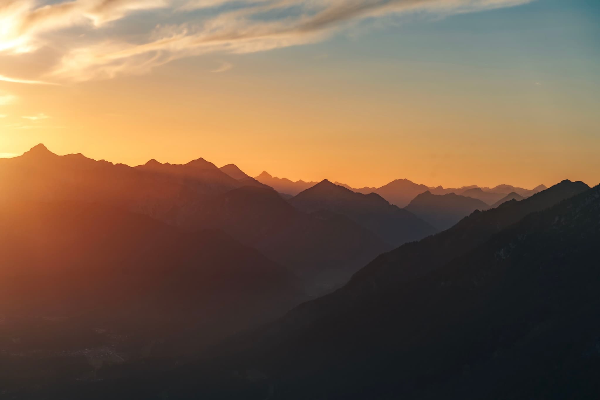 A mountain range silhouetted against a vibrant sunset sky with soft clouds