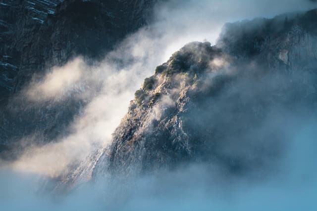 Sunlit mountain ridge emerging through swirling mist and low clouds