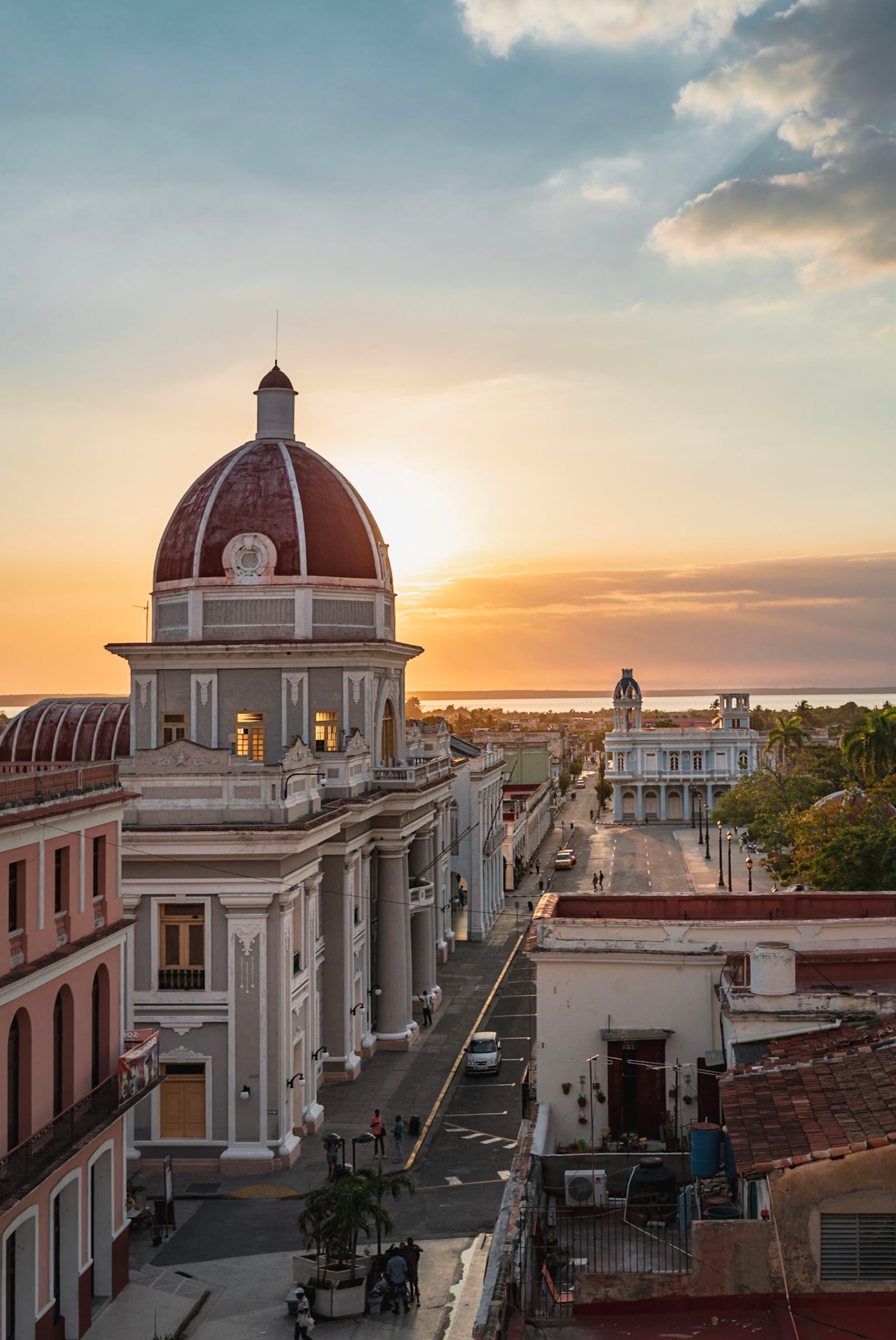 Historic domed building and surrounding town bathed in warm sunset light, viewed from an elevated vantage point along a main street leading toward the horizon
