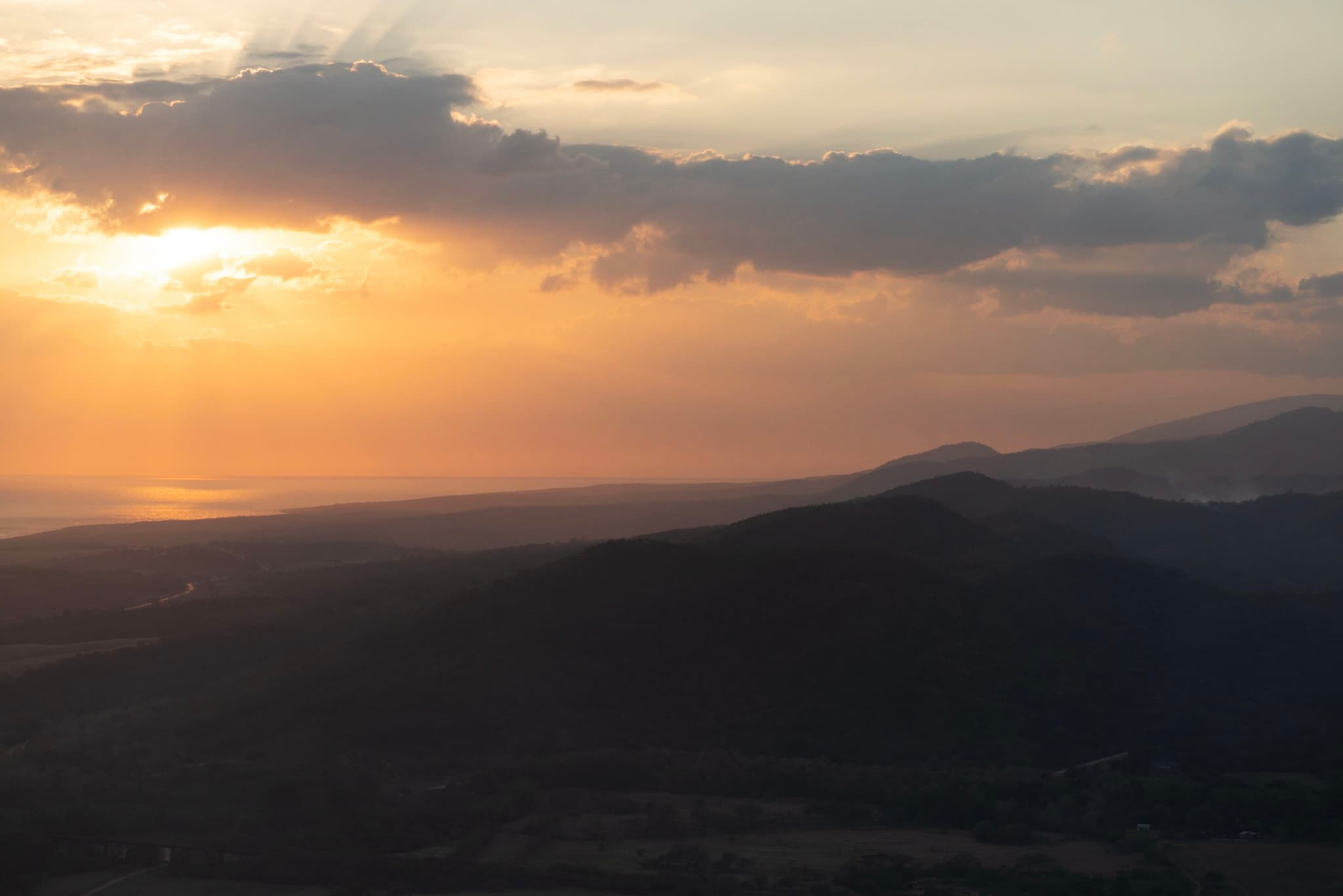 Sun setting through clouds over layered mountain ridges fading into the hazy horizon