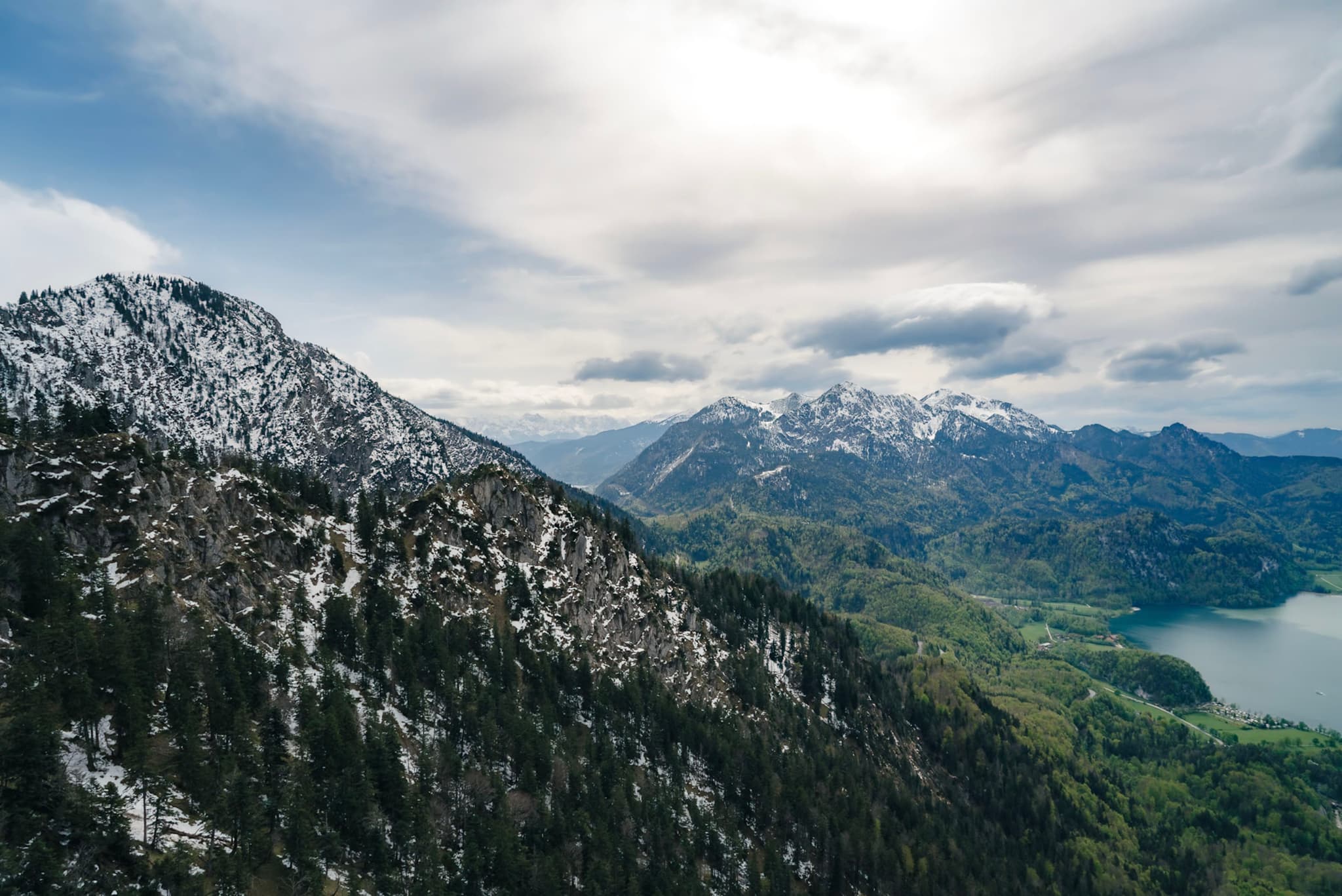 A mountainous landscape with snow-capped peaks, lush green valleys, and a partially cloudy sky