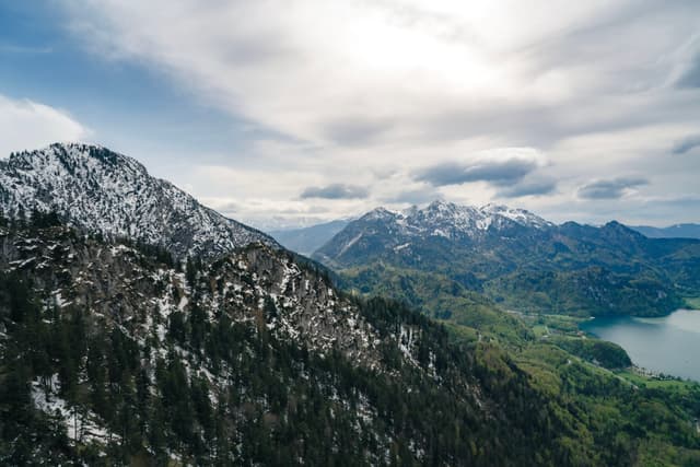 A mountainous landscape with snow-capped peaks, lush green valleys, and a partially cloudy sky