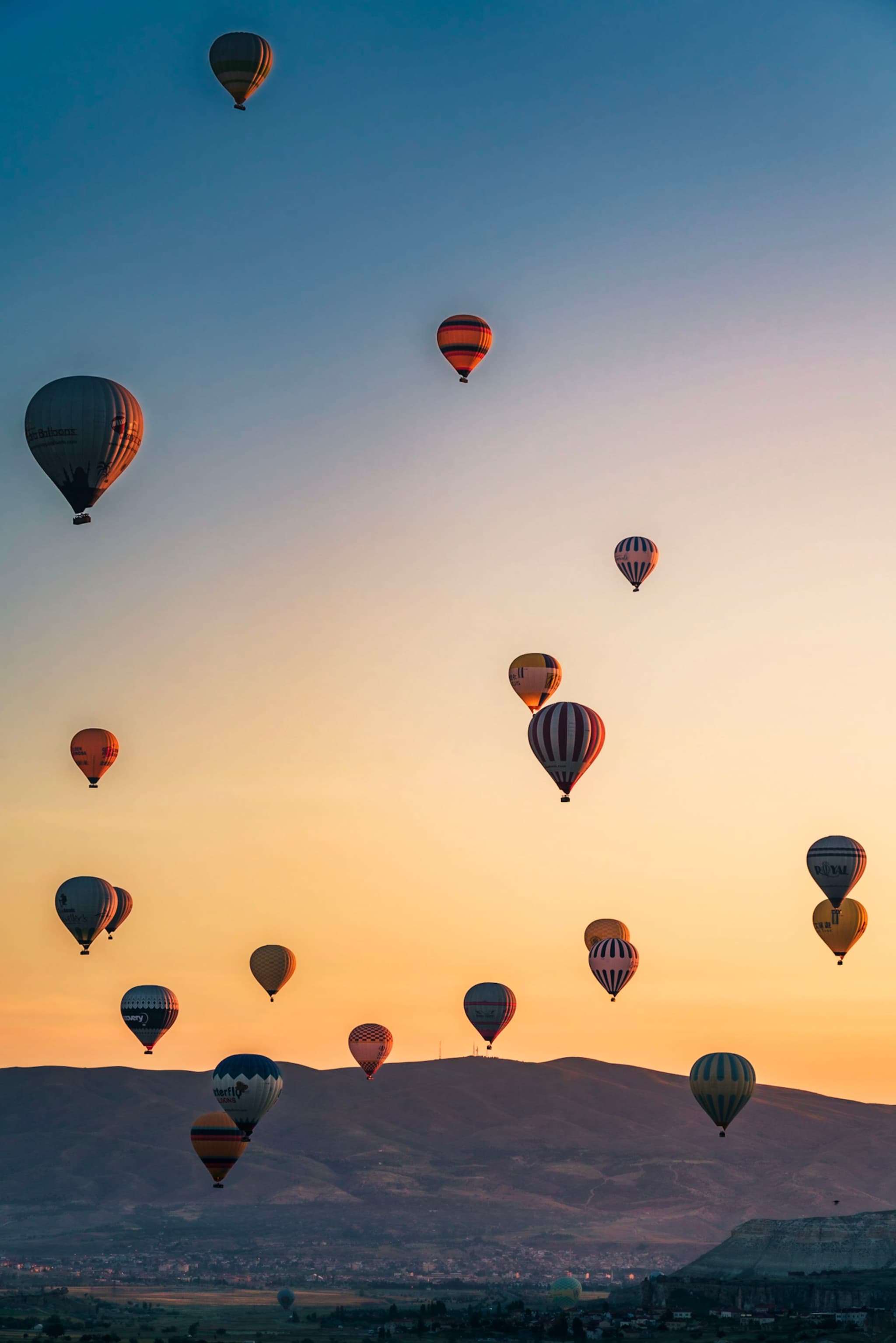 Hot air balloons floating in the sky during a colorful sunset over a mountainous landscape