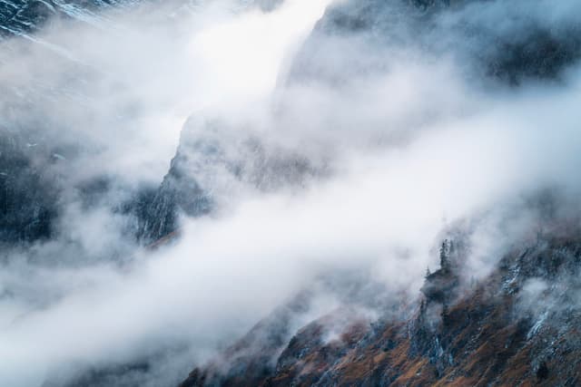 Jagged mountain slopes partly obscured by drifting white mist and low clouds