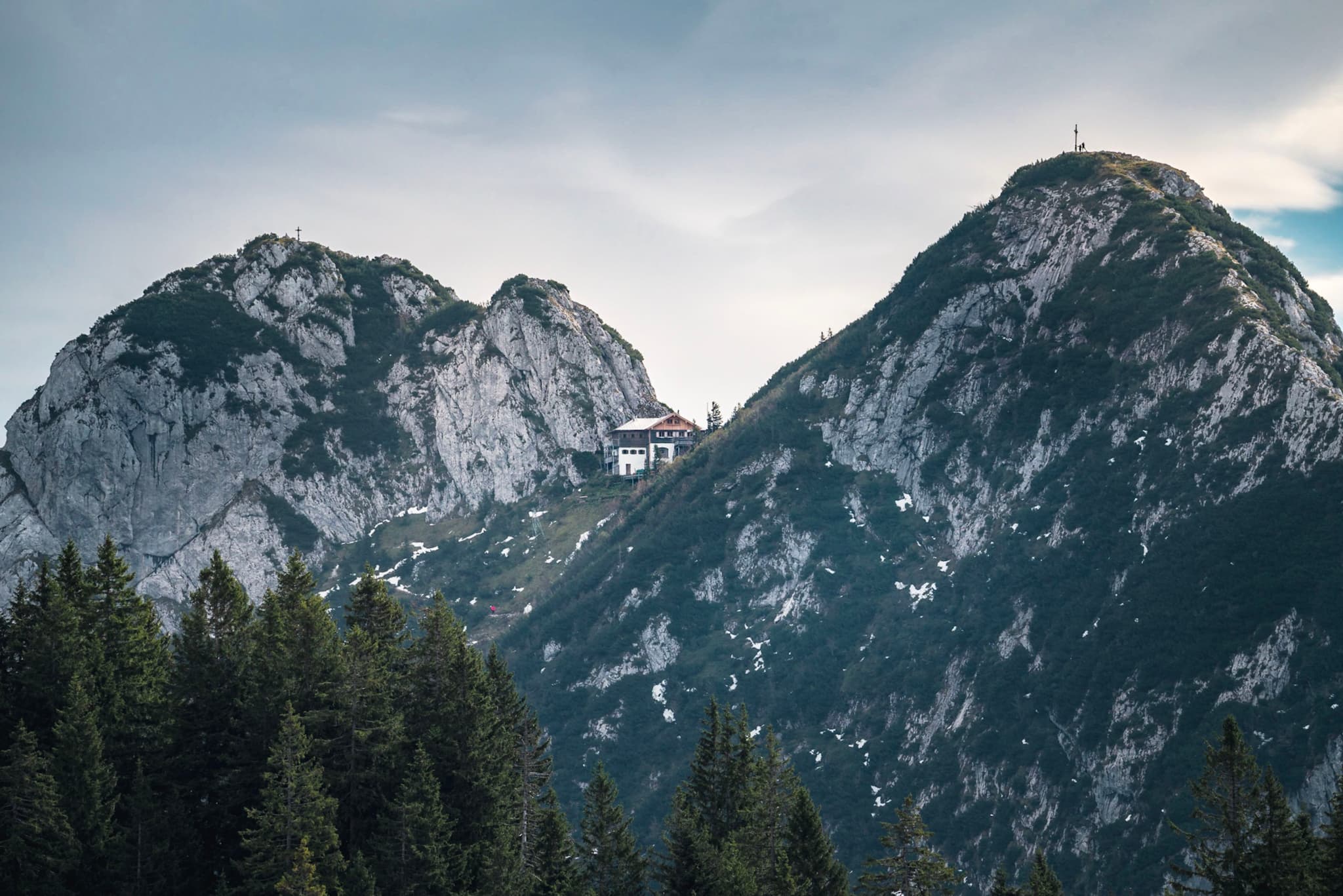 Snow-dusted twin mountain peaks rising above dense evergreen forest under a cloudy sky