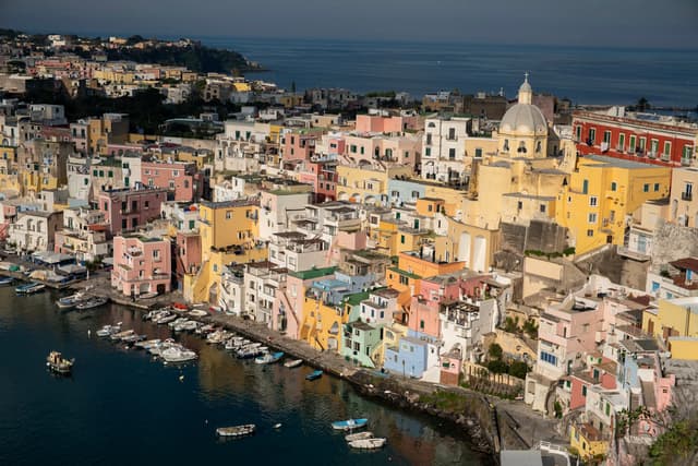 Colorful coastal town with tightly packed buildings descending to a small harbor lined with moored boats along calm blue water