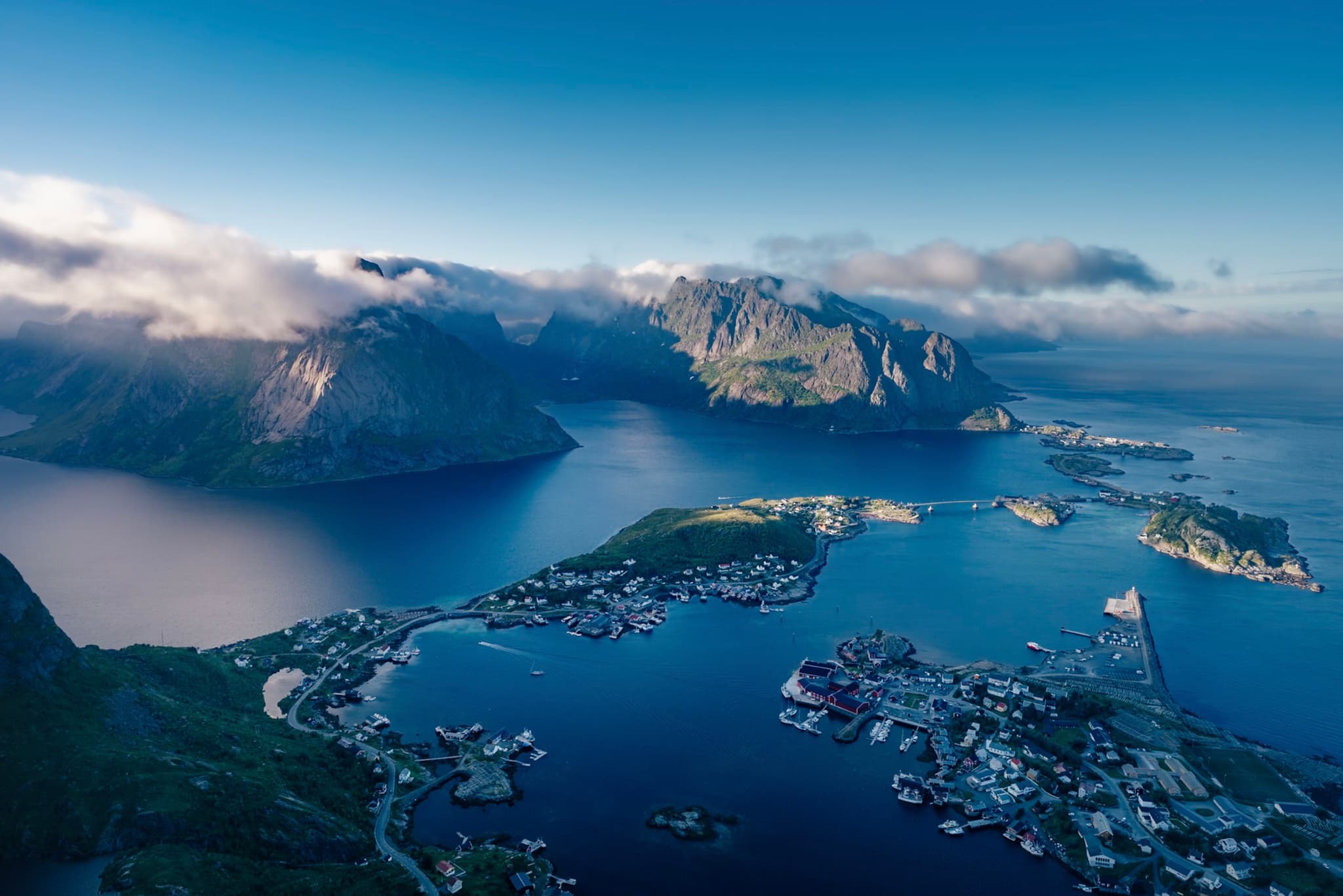 A scenic coastal landscape featuring a cluster of islands surrounded by deep blue water, with rugged mountains in the background and a partly cloudy sky