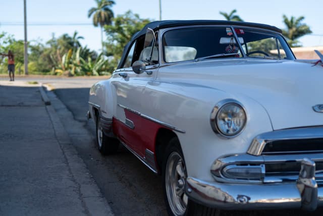 White and red vintage car parked on a sunny street with palm trees in the background