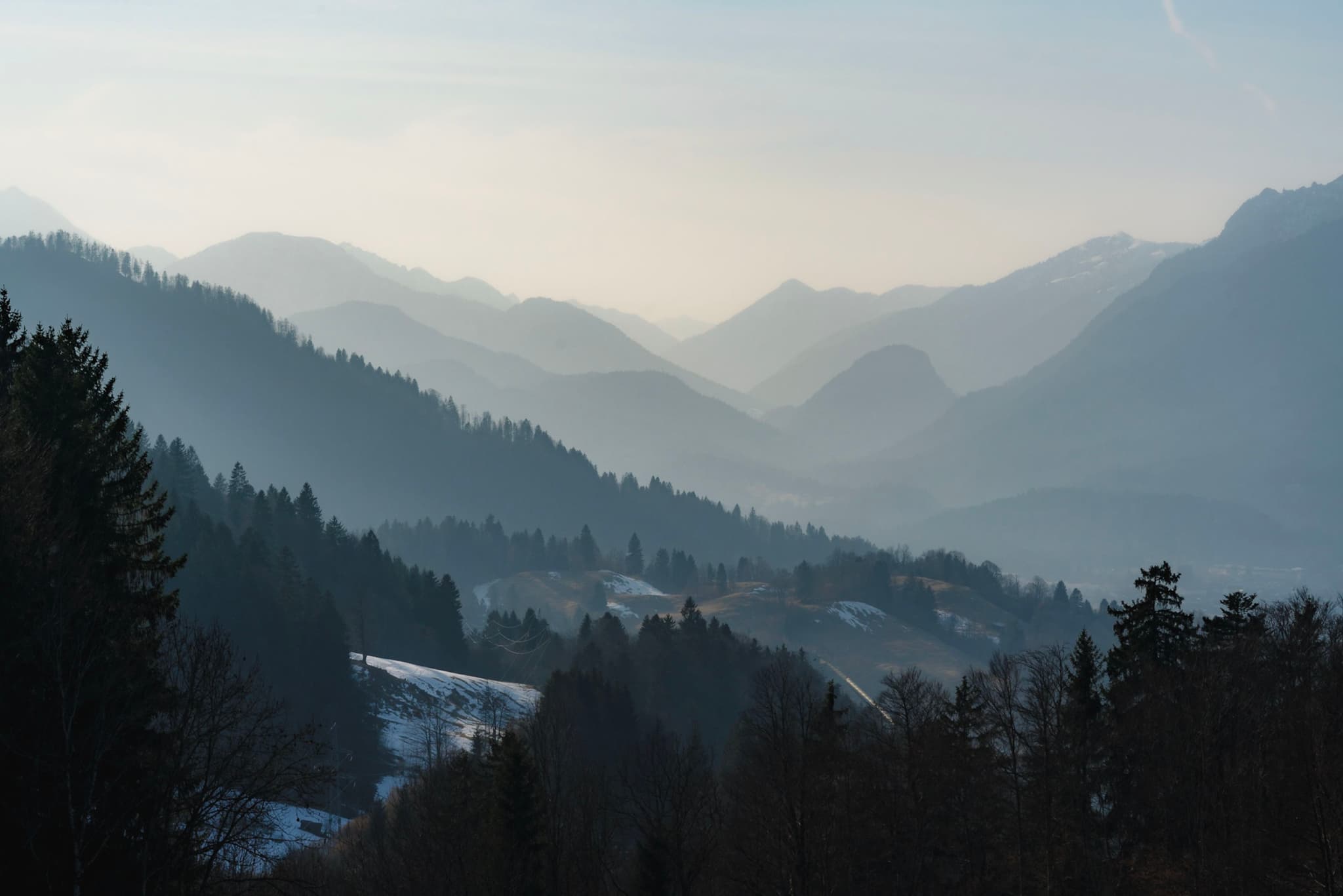 A serene mountain landscape with layers of misty hills in the background and a forested area in the foreground