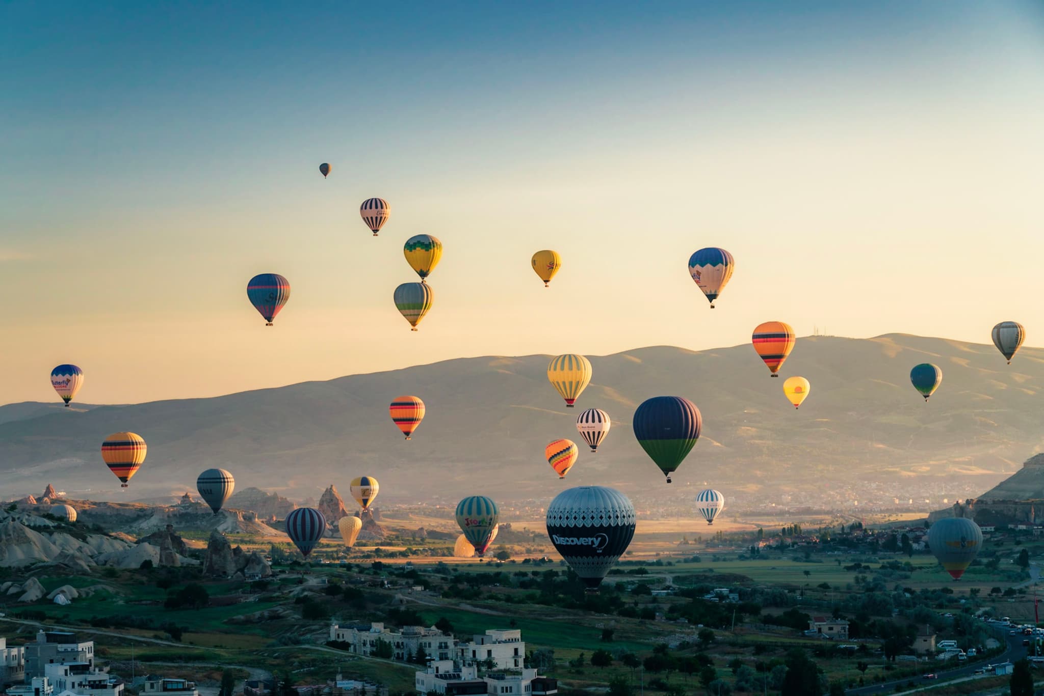 Hot air balloons floating over a scenic landscape with mountains in the background during sunrise or sunset