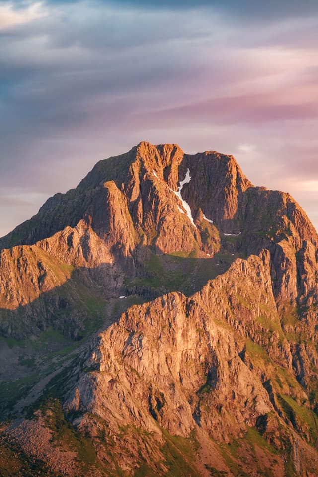 A majestic mountain peak bathed in warm, golden sunlight under a sky with soft, colorful clouds