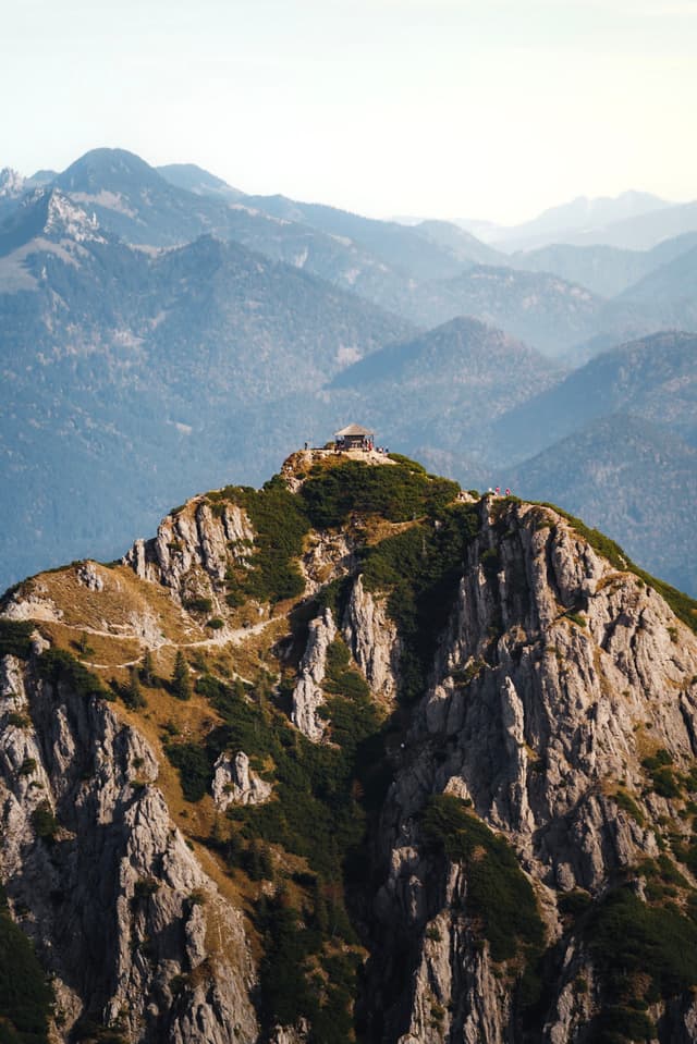 Jagged foreground summit with patches of greenery rising above hazy layers of distant mountain ridges