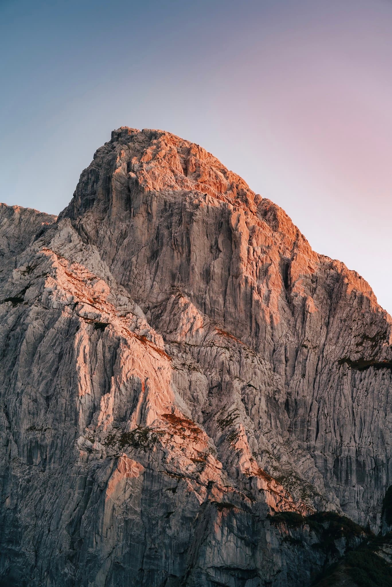 Towering rocky mountain peak glowing with warm light against a clear gradient sky