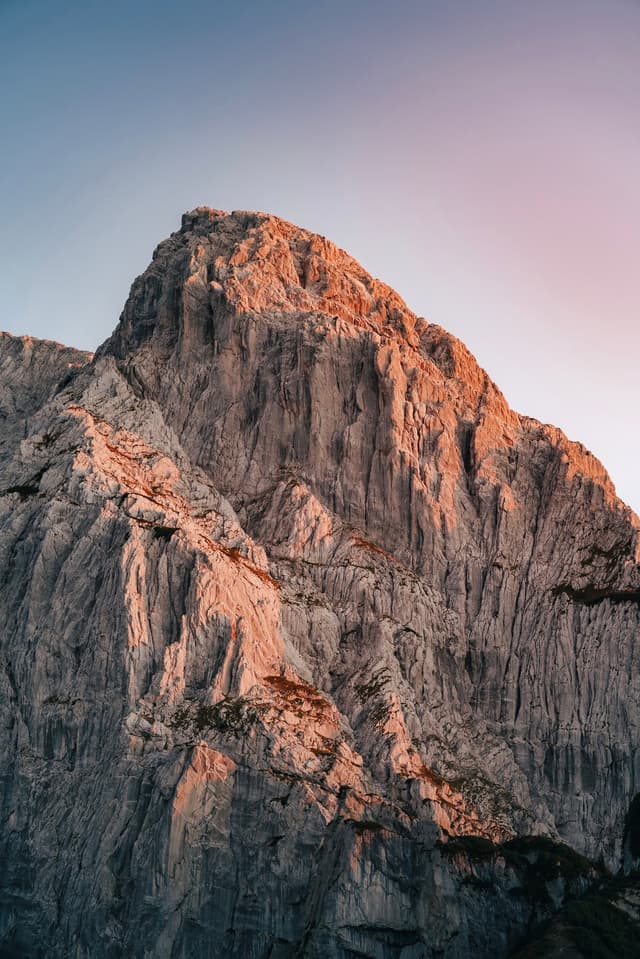 Towering rocky mountain peak glowing with warm light against a clear gradient sky