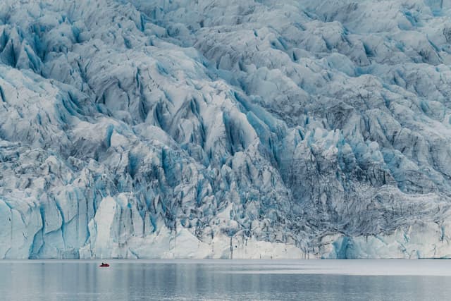 towering blue glacier wall rising above calm icy water with a tiny boat emphasizing the massive frozen landscape