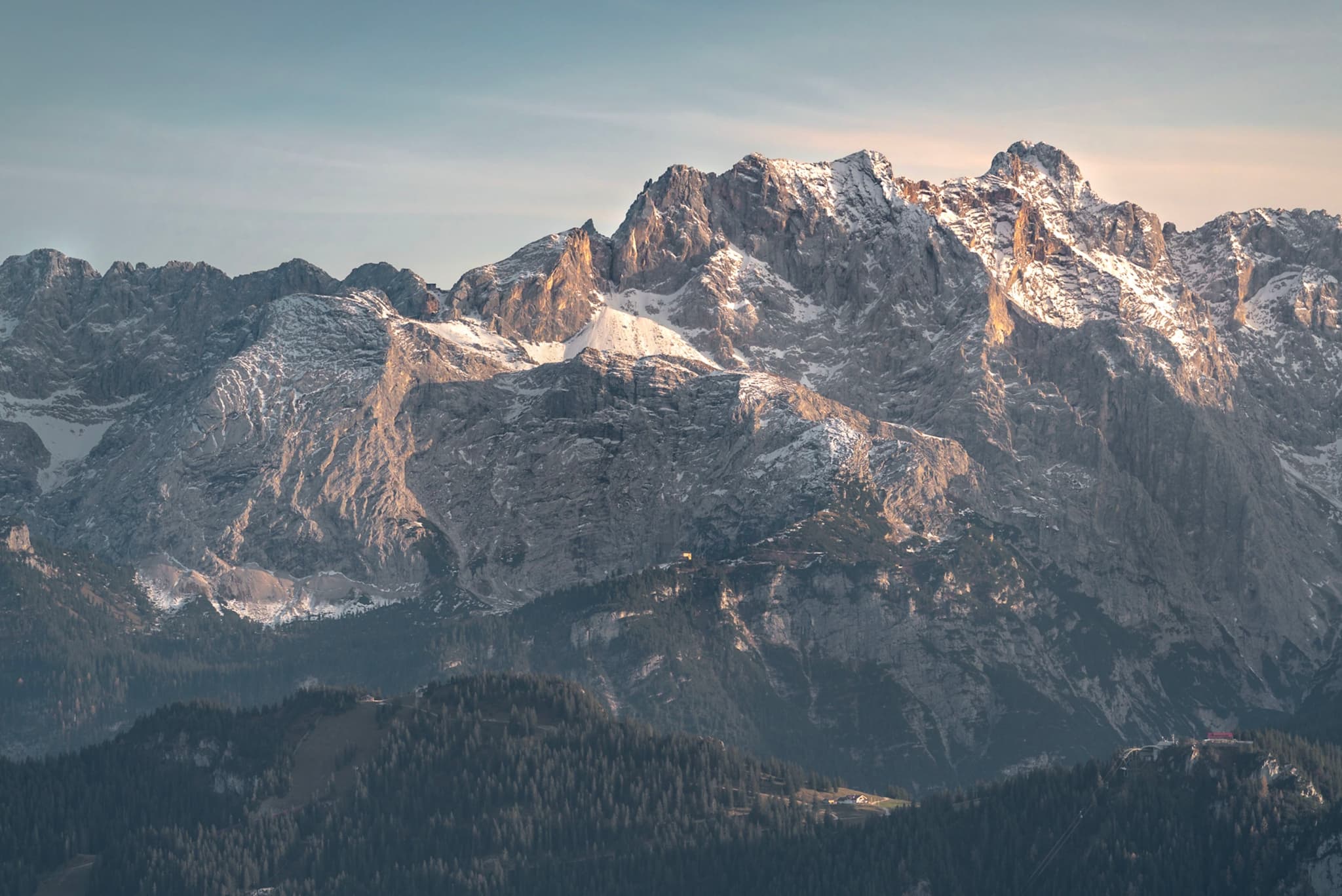 Snow-dusted alpine mountains rise above darker forested foothills under a clear sky