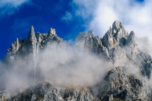 Jagged rocky mountain peaks piercing low clouds against a deep blue sky