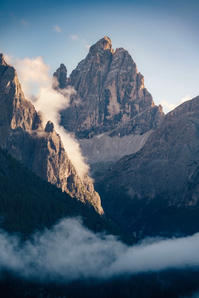 A majestic mountain peak surrounded by clouds, with a clear blue sky in the background