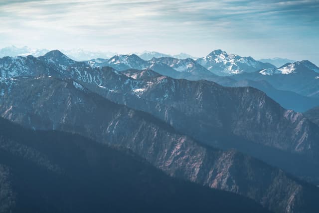 Layered blue ridgelines receding into distant snow-capped mountains under a hazy sky